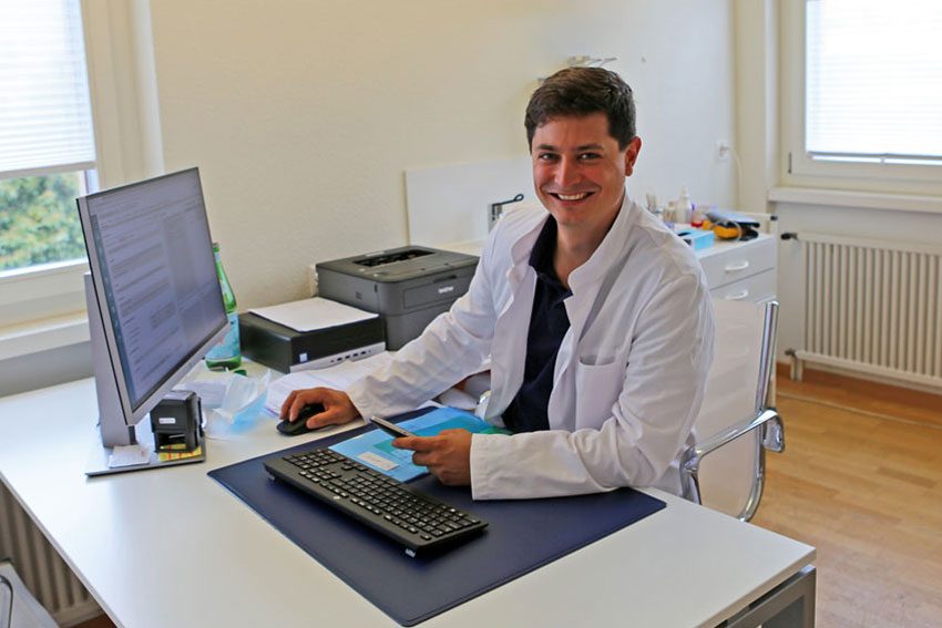 Dr. med. Tim Weitkunat, Facharzt für Allgemeine Innere Medizin FMH, an seinem Arbeitsplatz im Sprechzimmer der Gemeinschaftspraxis Wettingen